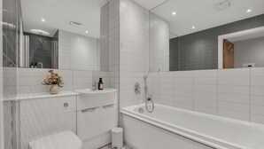A modern bathroom with a toilet, sink, and bathtub. - Cozy London Apartment With City Views (London)