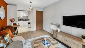 A modern living room with a sofa, coffee table, and a TV. There is a dining area with chairs and a table, and a kitchen in the background. - Cozy London Apartment With City Views (London)