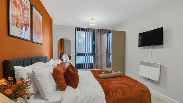 Une chambre d’hôtel équipée d’un lit, d’une télévision, d’un radiateur et d’une fenêtre avec des stores.
