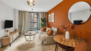 Un salon moderne avec un canapé, une table ronde en bois, un téléviseur et une grande fenêtre avec des rideaux.