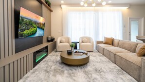 A modern living room with a flat-screen TV, two armchairs, a sofa, a round coffee table, and a chandelier. - 2406 - Great Family Home Near Disney, Pool. (Kissimmee)