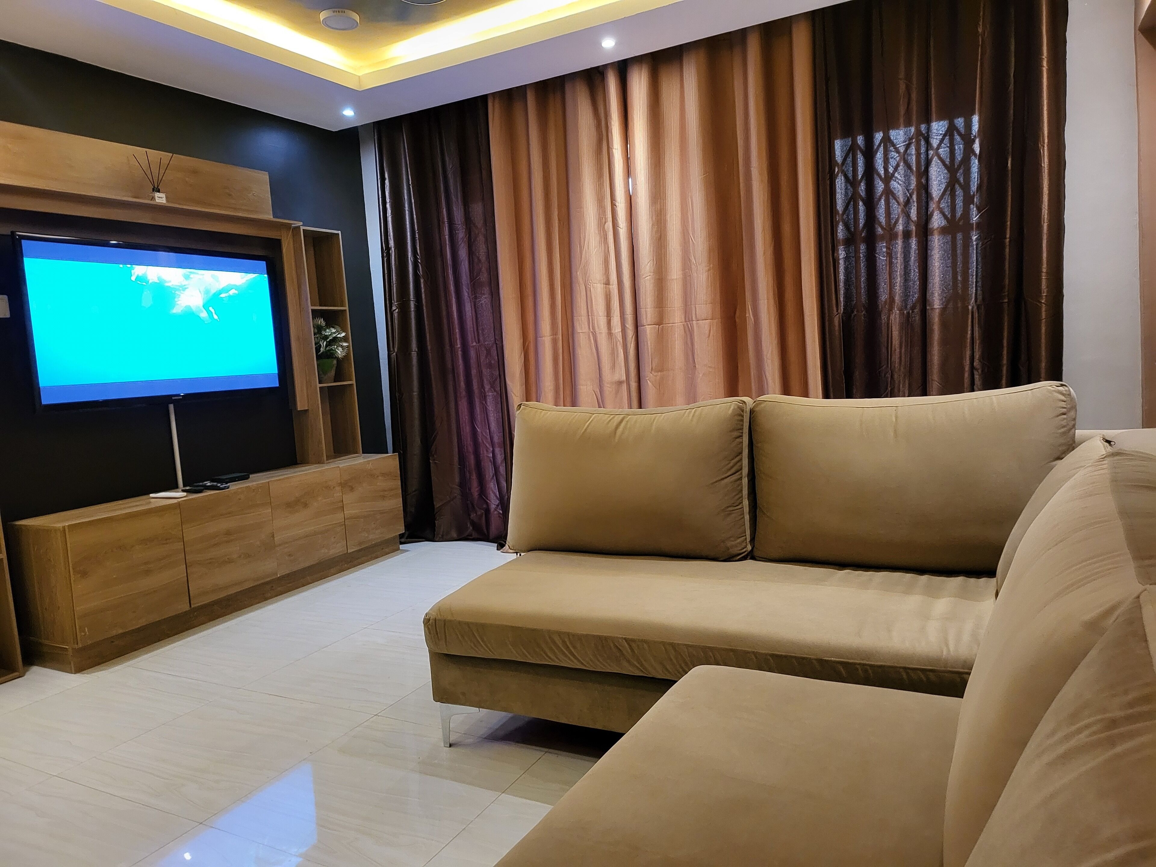 A modern living room with a large flat-screen TV, a beige sofa, and a wooden entertainment unit.