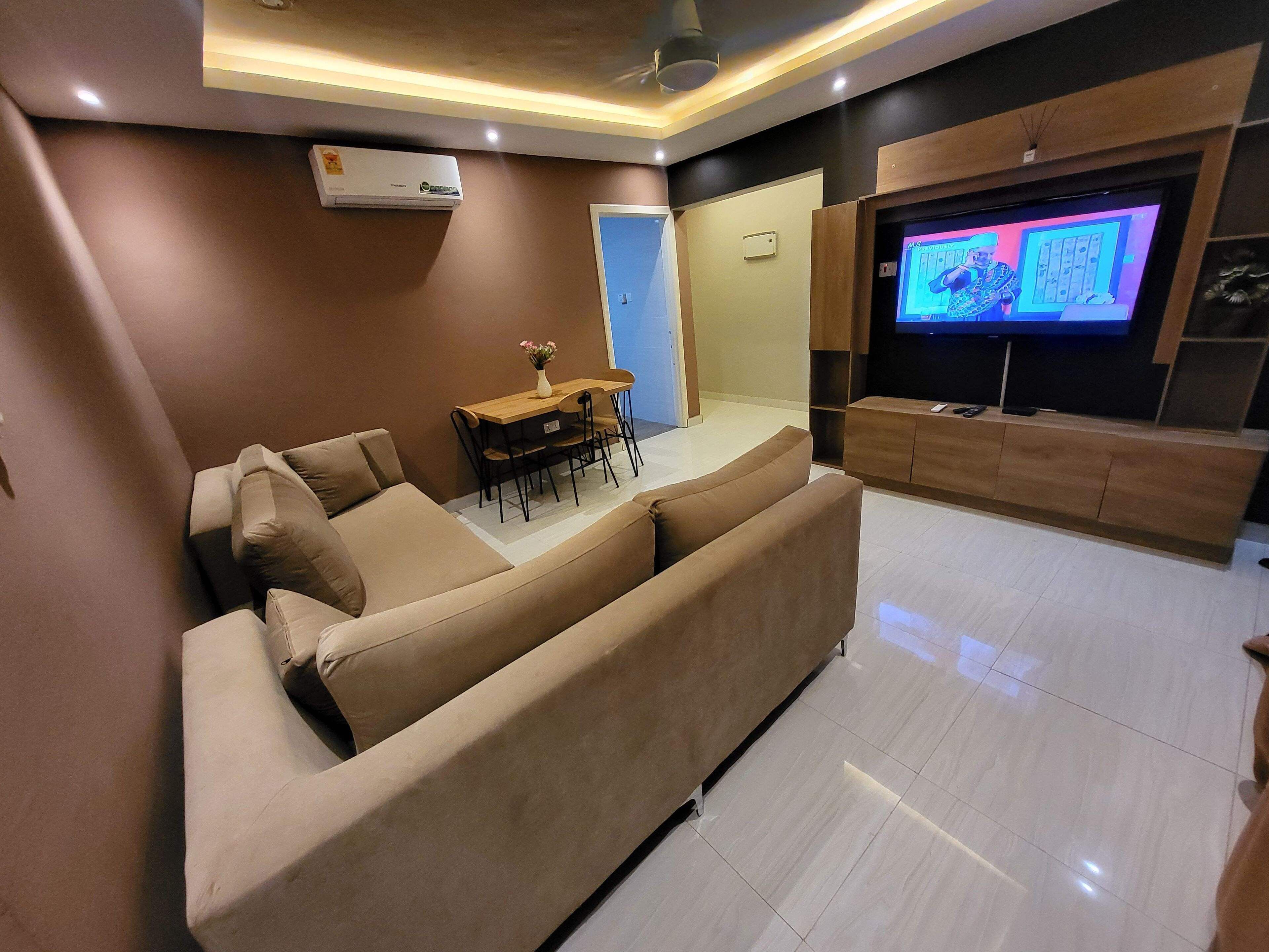 A modern living room with a large flat-screen TV, a sofa, a dining table, and an air conditioning unit.