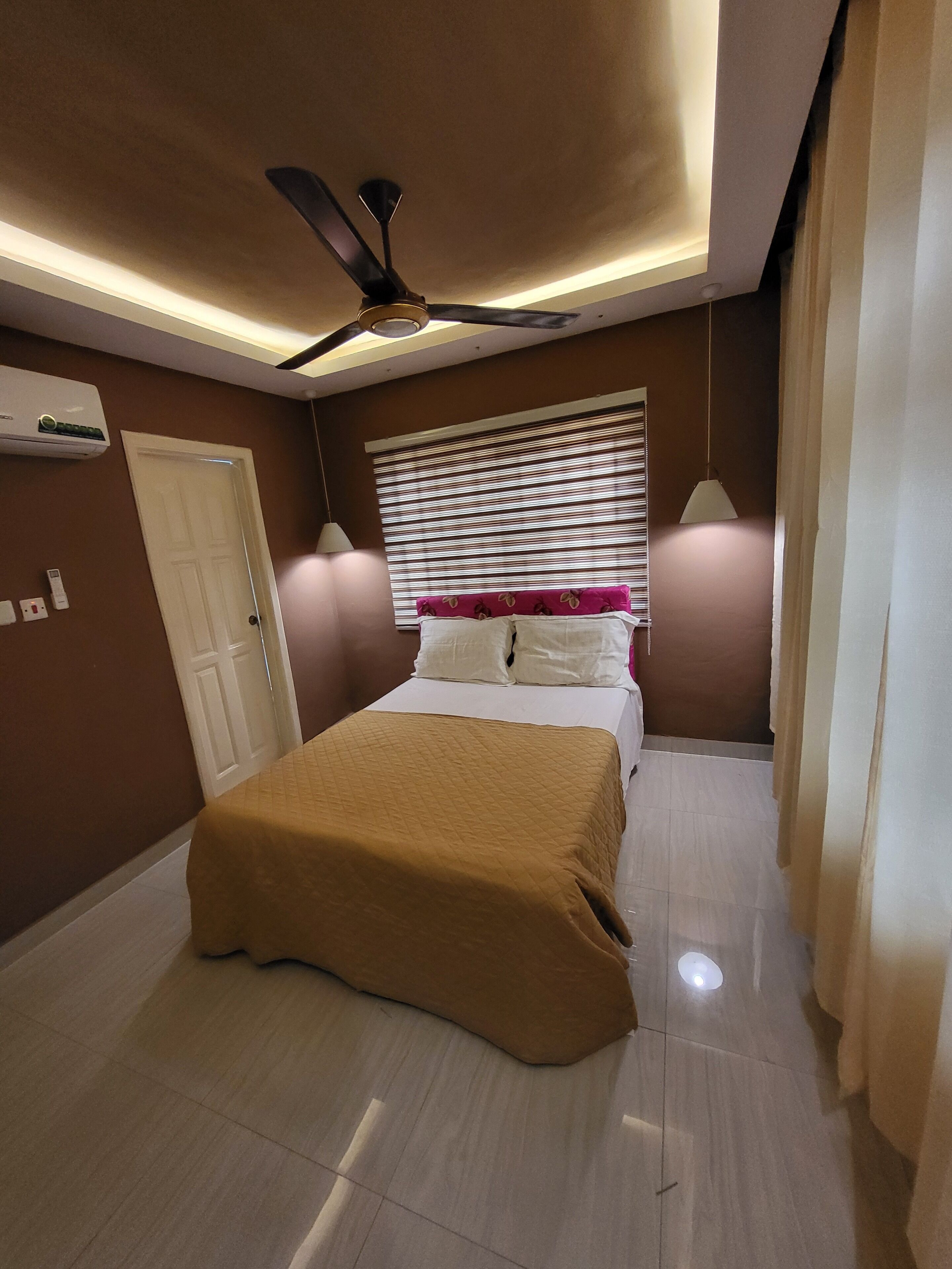 Un dormitorio con cama, ventilador de techo, aire acondicionado y ventana con persianas.