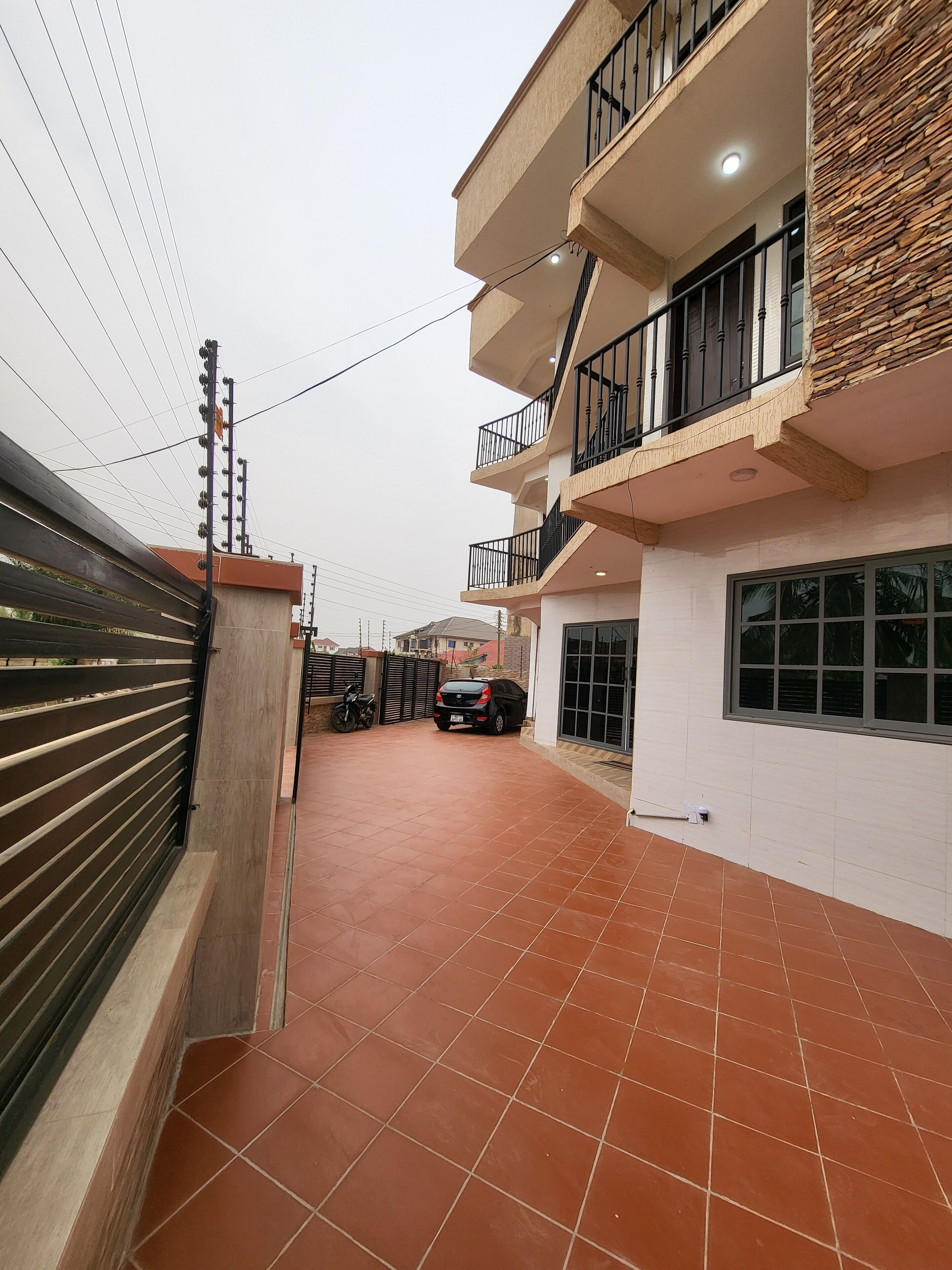 A residential building with a tiled patio, a car parked outside, and a gated entrance.