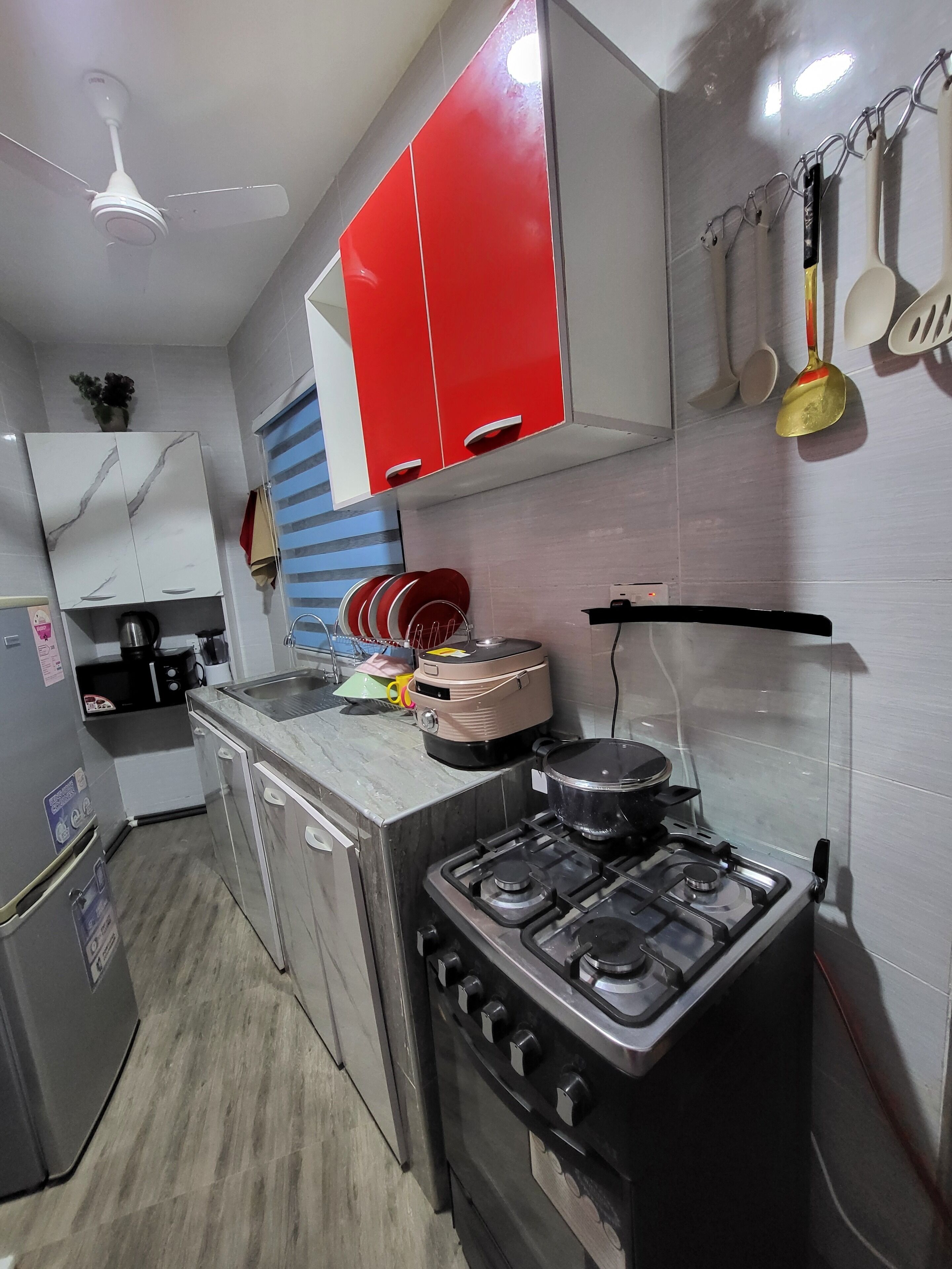 A kitchen with a gas stove, oven, and a red and white cabinet. There is a ceiling fan, a microwave, and a sink.