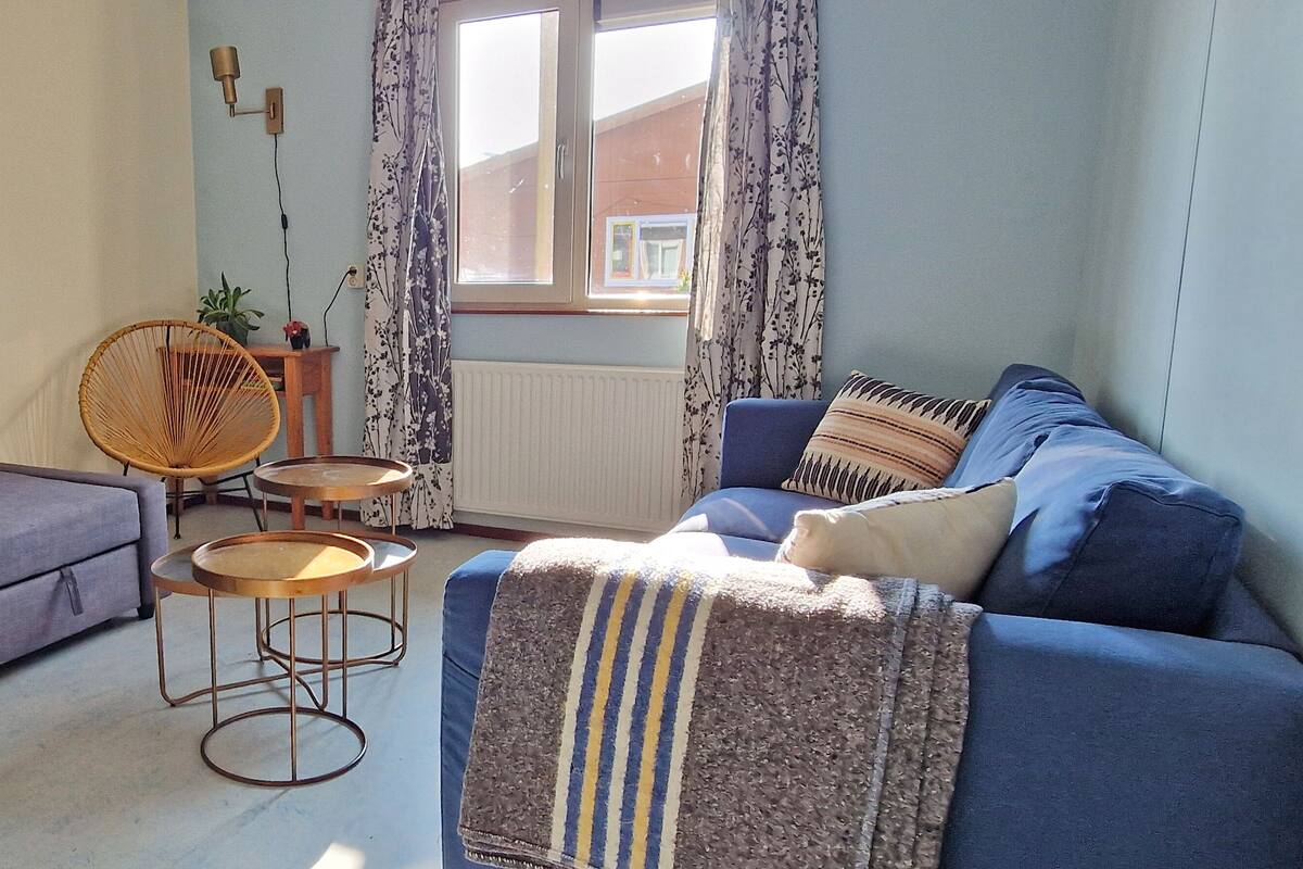 A living room with a grey sofa, a blue sofa, a round wooden coffee table, and a wicker chair.