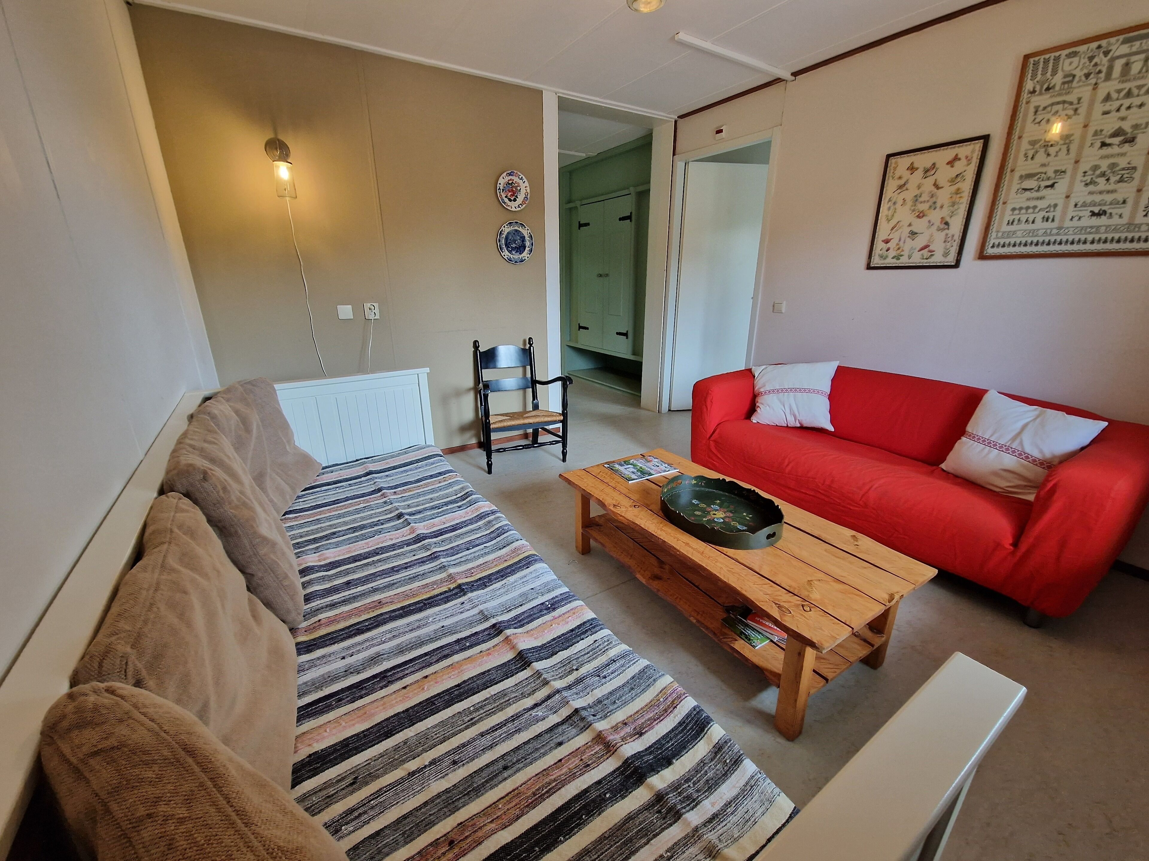 A living room with a striped rug, a red sofa, a wooden coffee table, and a white radiator.