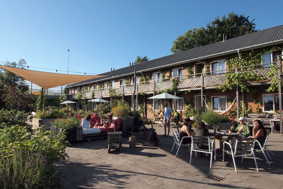 An outdoor patio area with seating arrangements, umbrellas, and a building with a tiled roof in the background.