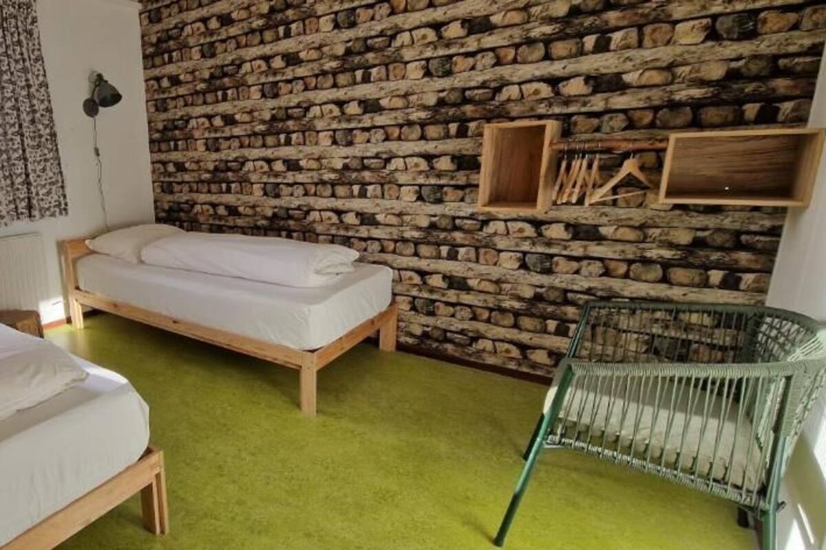 A room with two wooden beds, a green carpet, a stone wall, and a green chair.