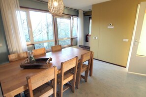 Zona pranzo con tavolo e sedie in legno, ampie finestre e lampadario.