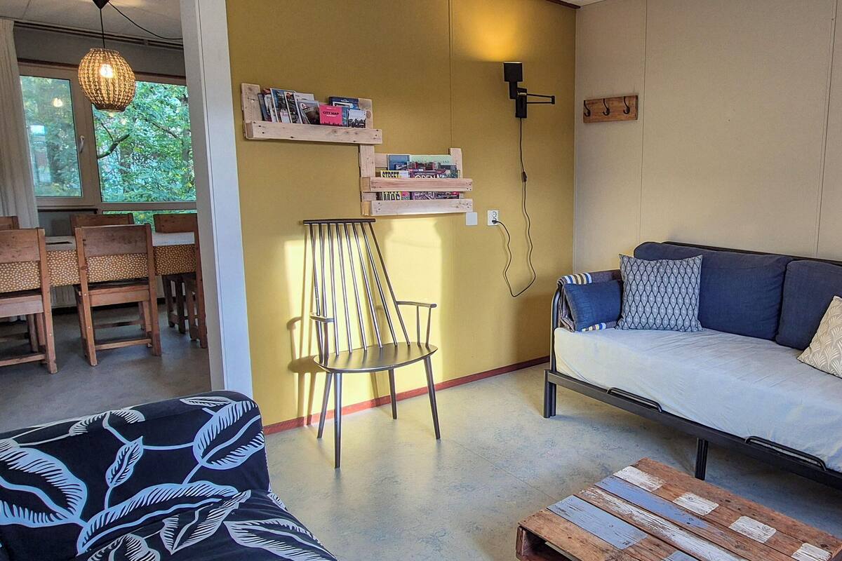 A cozy living room with a sofa, a patterned armchair, a wooden coffee table, and a bookshelf against the wall.