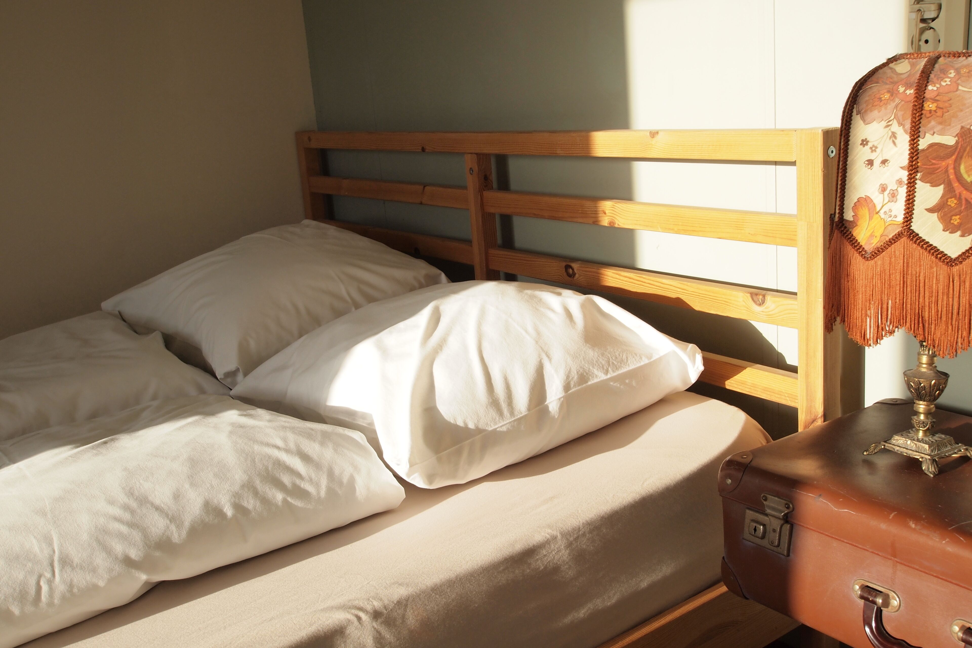 A bed with a wooden headboard, a suitcase, and a lamp on a bedside table.