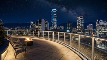 Terraço no telhado com lareira, área de estar e vista noturna da cidade.
