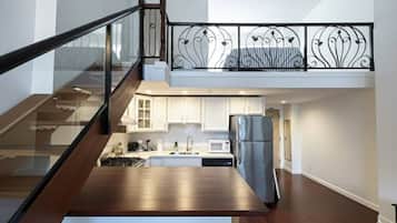 Een moderne keuken met een roestvrijstalen koelkast, witte kasten en een glazen balustrade met uitzicht over de ruimte.