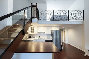 Cozinha moderna com geladeira de aço inoxidável, armários brancos e guarda-corpo de vidro com vista para o ambiente.