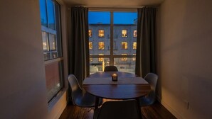 Ein Eckzimmer mit Tisch und Stühlen, großen Fenstern und Blick auf Gebäude.