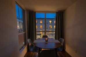 Ein Eckzimmer mit Tisch und Stühlen, großen Fenstern und Blick auf Gebäude.