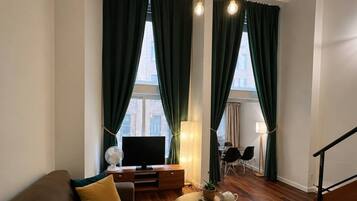 Uma sala de estar moderna com sofá, televisão, abajur e área de jantar com cadeiras.