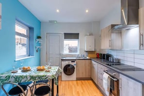 A compact kitchen with a washing machine, a sink, and a stove. There is a window with a view of the outside. - The Kensington House (Liverpool)