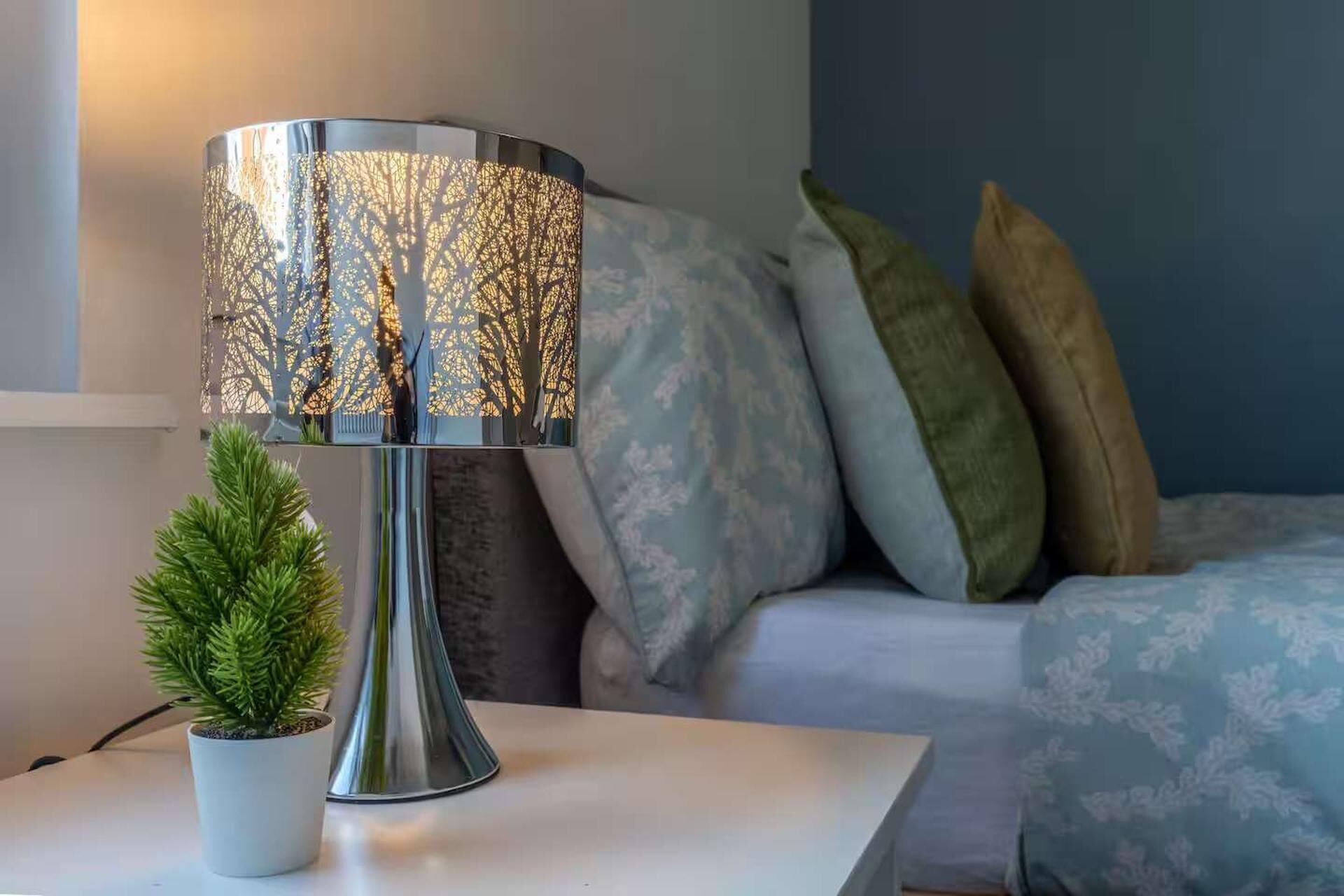 Une lampe dont l’abat-jour est orné d’un motif d’arbre, une petite plante en pot et un canapé avec des coussins à motifs.