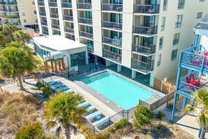 A multi-story hotel with a rooftop pool, outdoor seating, and a landscaped area with palm trees. - Oceanfront 3-bedroom end unit in sought after Windy Hill Beach (North Myrtle Beach)