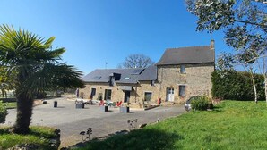 A stone building with a sloped roof, multiple windows, and a paved courtyard with outdoor seating.