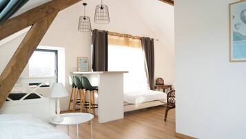 A cozy loft bedroom with a bed, a small desk, and a chair. There is a window with curtains, a lamp, and a framed picture on the wall.