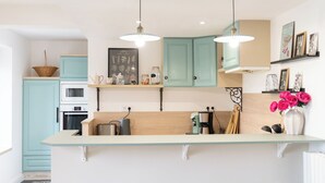 A modern kitchen with teal cabinets, a central island with stools, pendant lighting, and a patterned floor.