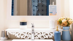 A bathroom with a white sink, a mirror, and a shower. There is a towel rack and a vase with flowers on the sink.