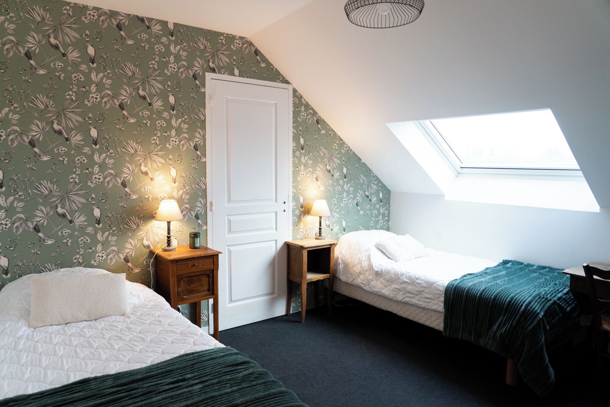 Une chambre avec deux lits, une lucarne et un papier peint à motifs floraux.