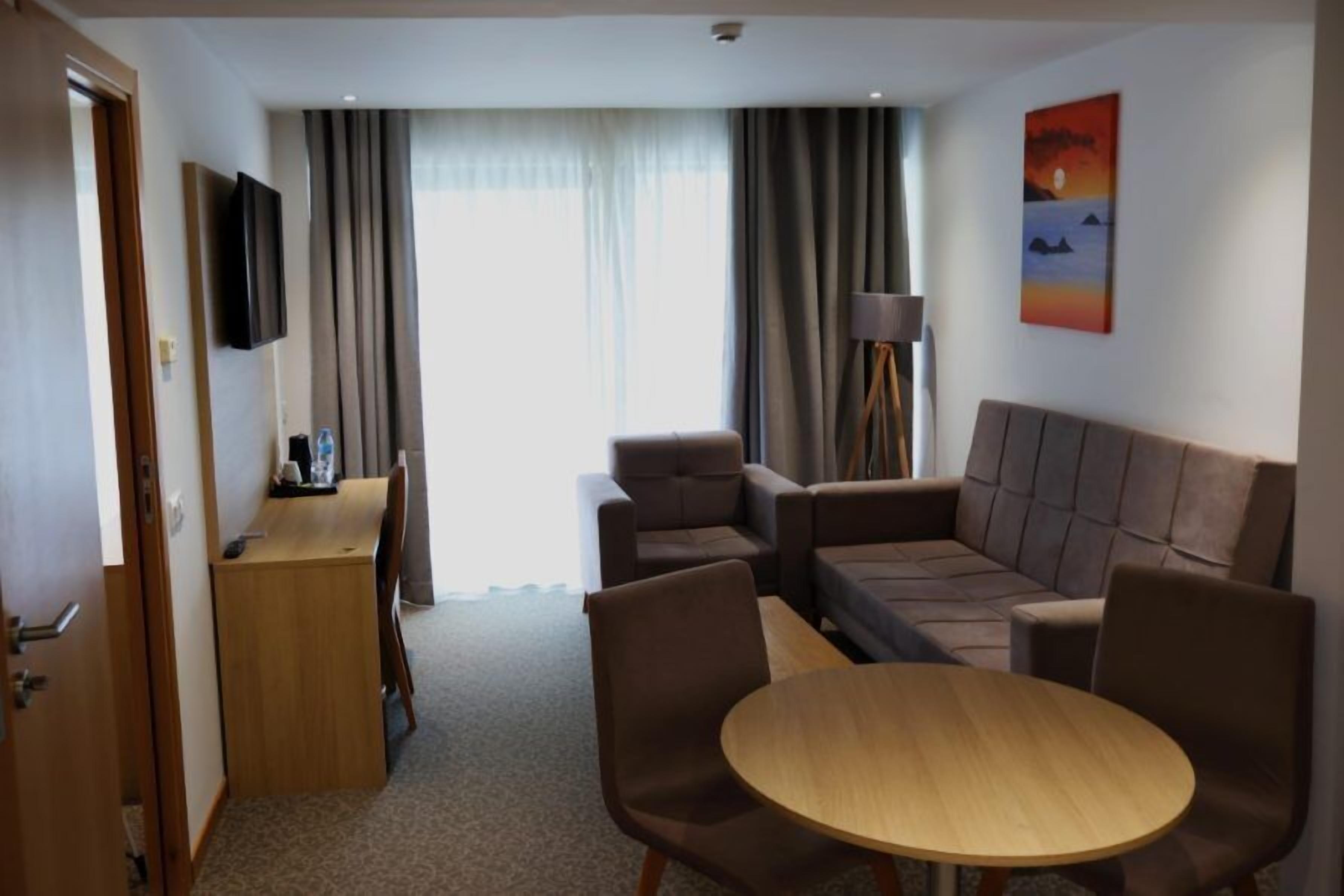 A hotel room with a sofa, a small table, a TV, and a painting on the wall.