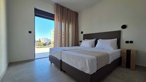 Ein modernes Hotelzimmer mit einem großen Bett, Blick auf die Stadt und einer Schiebetür.