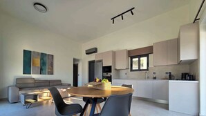 Eine moderne Küche mit weißen Schränken, ein Essbereich mit einem runden Holztisch und Stühlen, sowie ein graues Sofa im Wohnbereich.