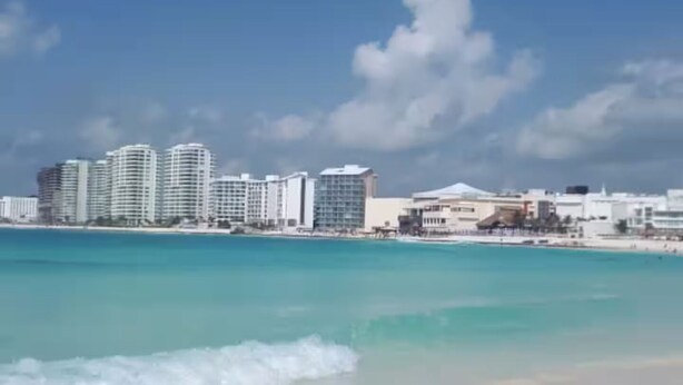 Ein Strand mit klarem türkisfarbenem Wasser und einer Stadtansicht im Hintergrund.