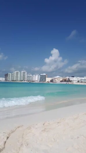 A beach with clear turquoise water and a city skyline in the background. - Salvia Beach Front Condo in Cancun's Hotel Zone (Cancún)