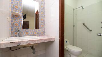 Un baño con piso de cerámica, lavamanos con espejo, inodoro y zona de ducha.