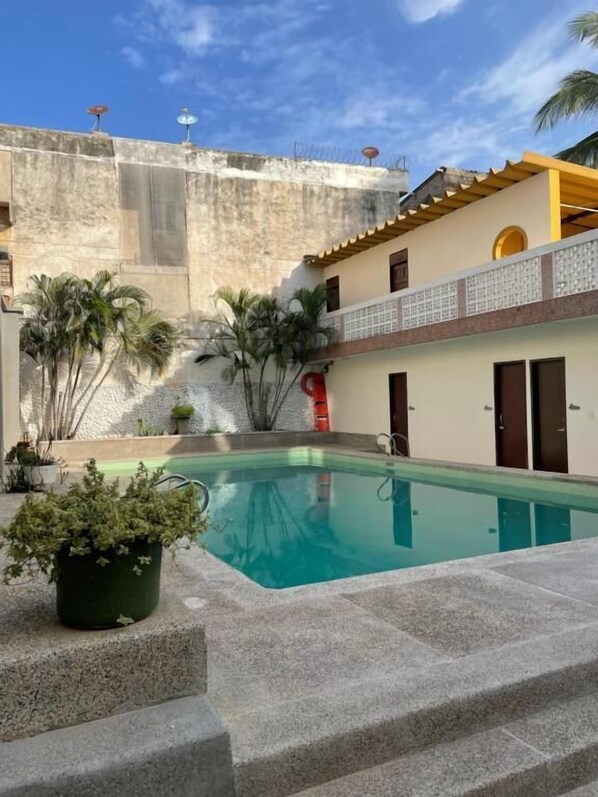 A swimming pool with a stone deck, a building with a balcony, and palm trees. - Hotel Skal Inn (Barranquilla)