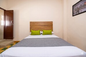A hotel room with a wooden headboard, two green pillows, a white bedspread, and a gray throw. - Hotel Skal Inn (Barranquilla)