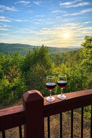Vista panoramica da un pontile in legno su un paesaggio boschivo, con due bicchieri di vino rosso.