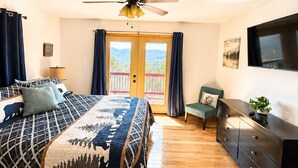 Un dormitorio con cama, ventilador de techo, cómoda, televisor y balcón con cortinas.