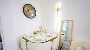 Un coin repas avec une table ronde, des chaises blanches et une horloge fixée au mur.