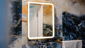 Une salle de bain avec un mur en marbre, un miroir avec un cadre doré et un porte-serviettes sur lequel est posée une serviette blanche.