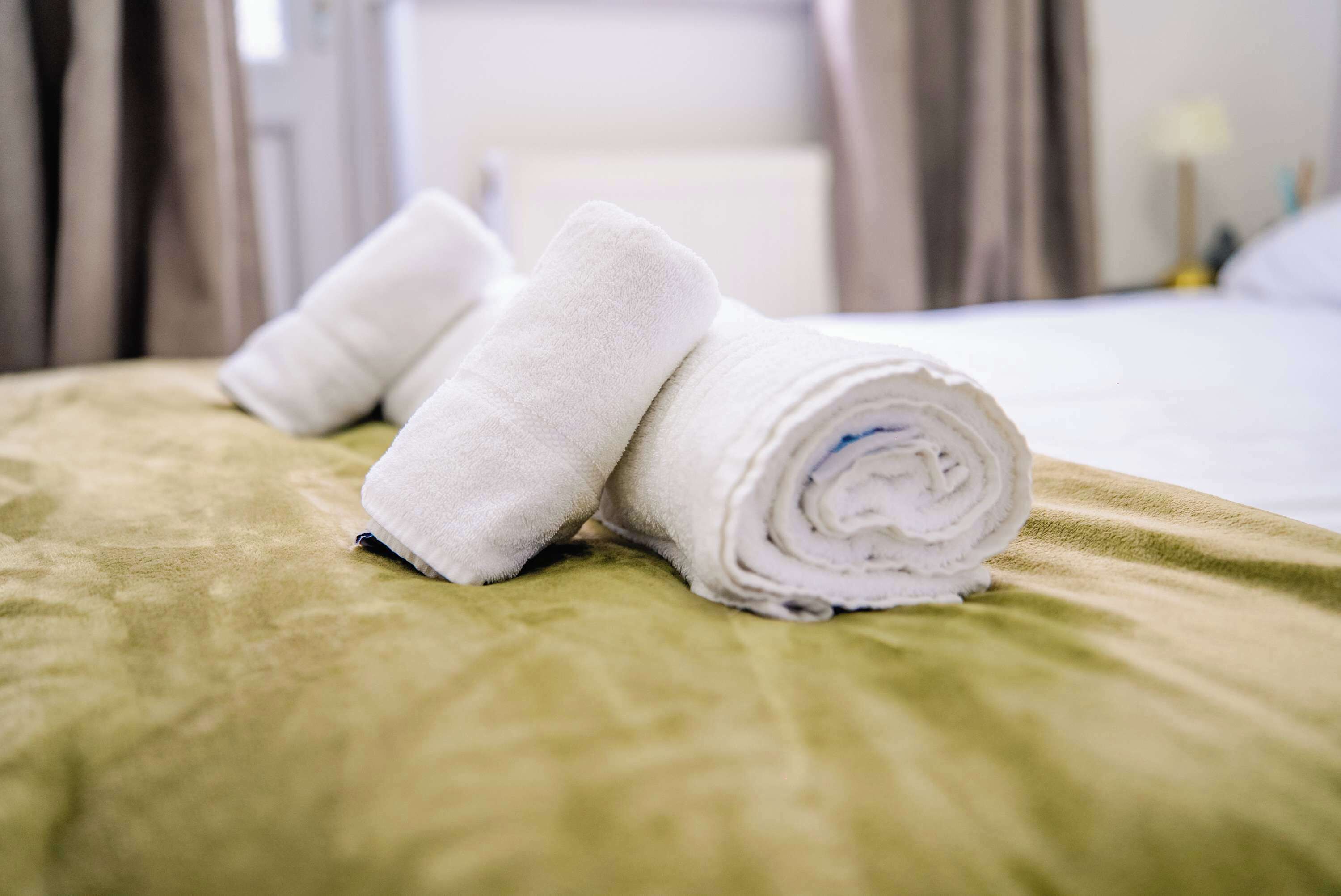 Een bed met netjes gevouwen witte handdoeken en een groene spreidek.