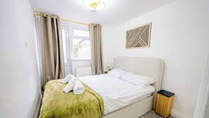 Un lit bien fait, recouvert d’une couverture verte, une table de chevet avec une lampe et une œuvre d’art géométrique accrochée au mur.