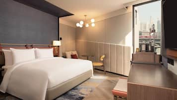Quarto de hotel moderno com uma cama grande, uma escrivaninha, uma cadeira, uma mesinha e vista para a cidade.