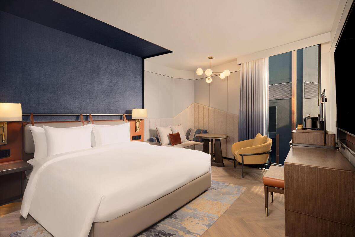 Habitación de hotel con una cama grande, un escritorio, una silla, un televisor y una ventana con cortinas.