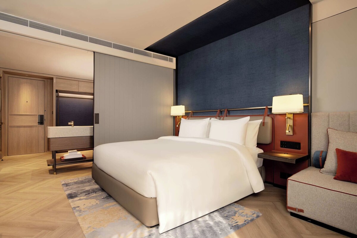 Ein modernes Hotelzimmer mit einem großen Bett, Nachttischen, einem Sofa, einem Schreibtisch und einem Kleiderschrank.
