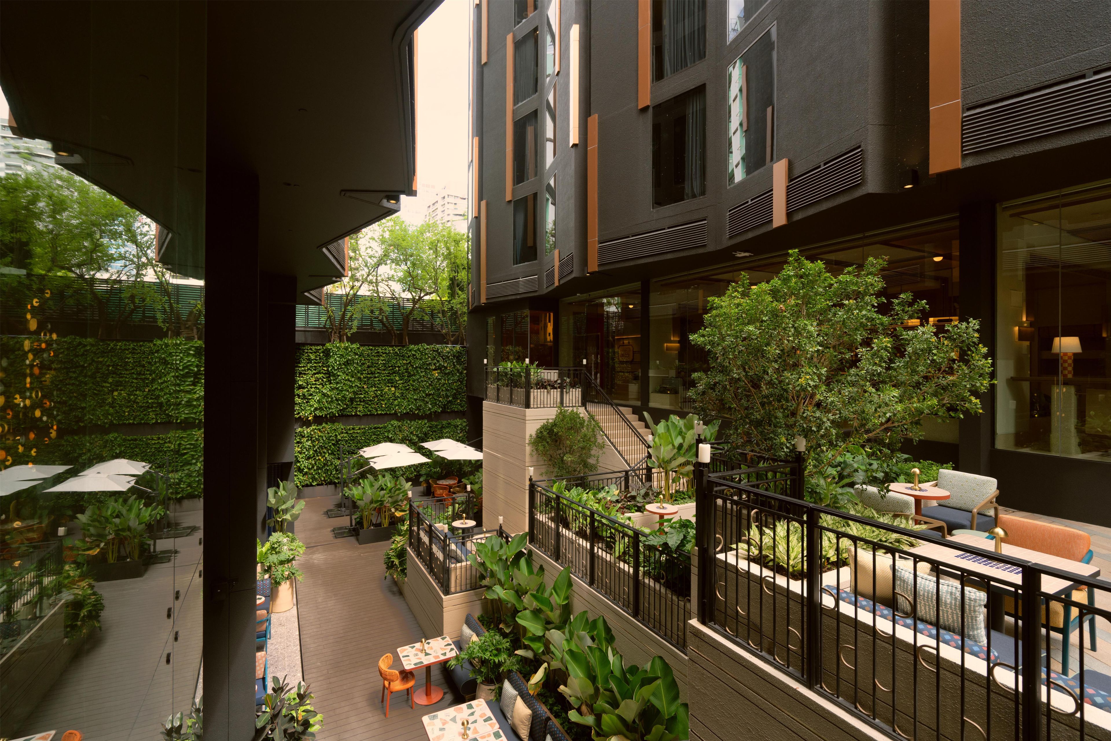 Um pátio ao ar livre com vários níveis, assentos, vegetação e vista para o interior do edifício.