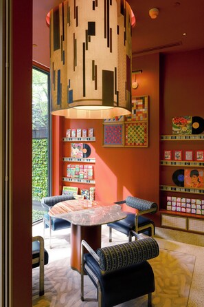 Ein Zimmer mit einem runden Tisch, Stühlen, einer deckenhohen Leuchte mit Muster und einer Wand mit Regalen, auf denen Schallplatten und Bücher präsentiert werden.